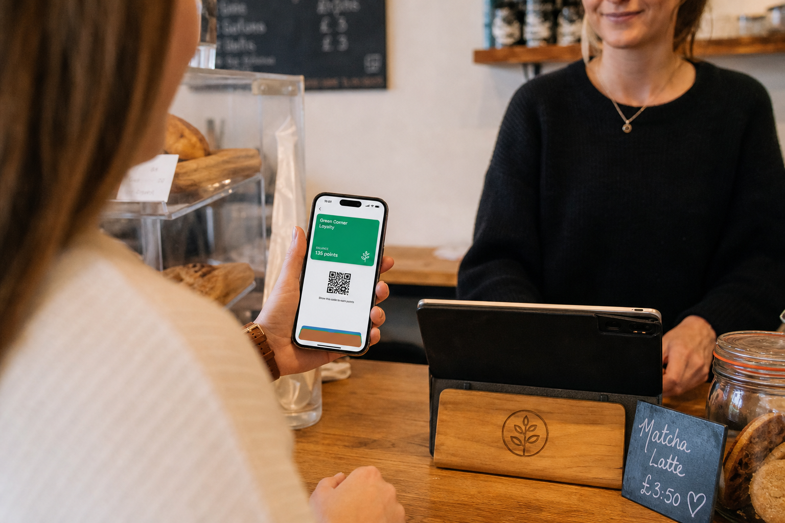 A customer holding up a phone showing a loyalty card saved in Apple Wallet at a cafe counter
