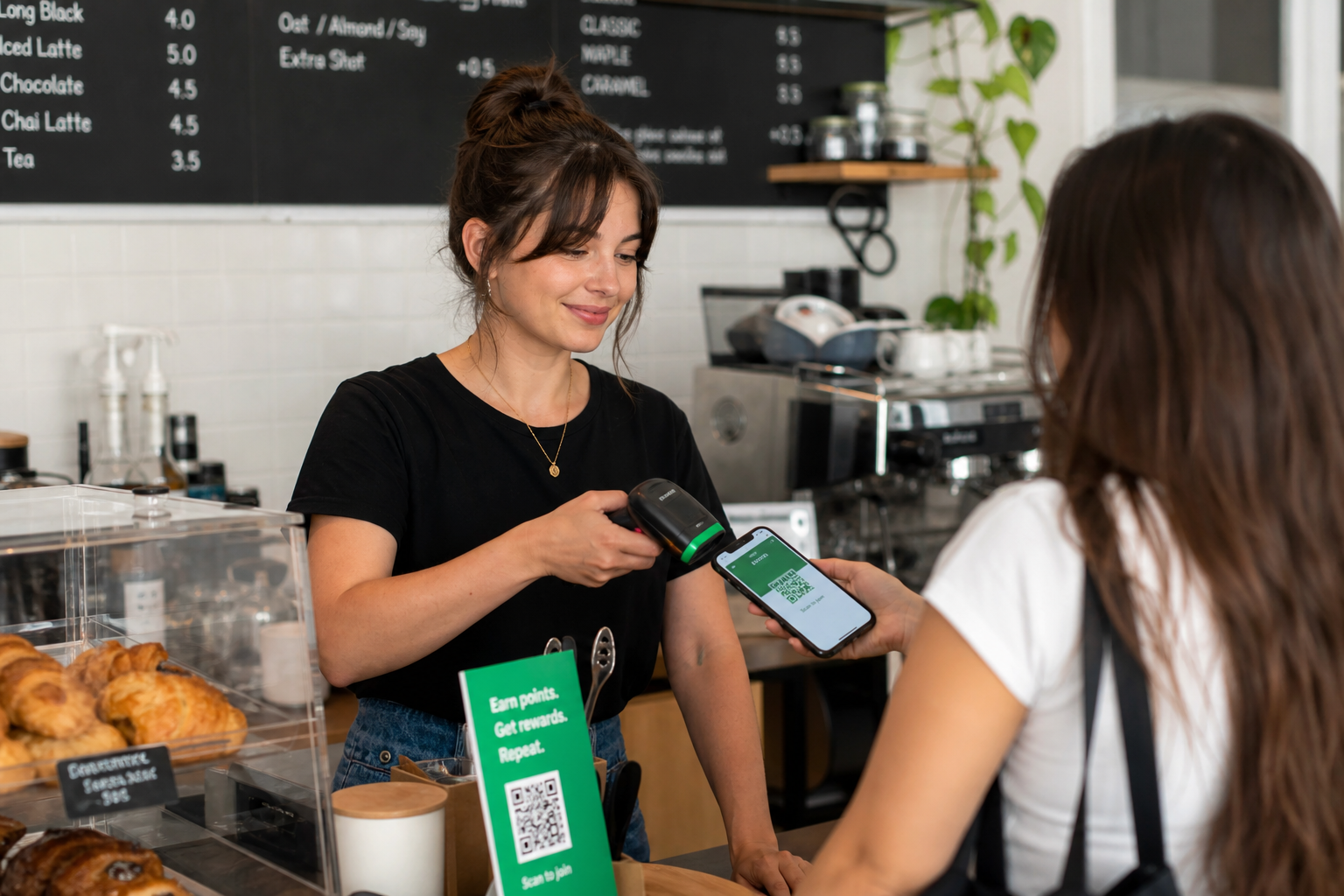 A barista at a small cafe counter scanning a customer's wallet pass on a phone